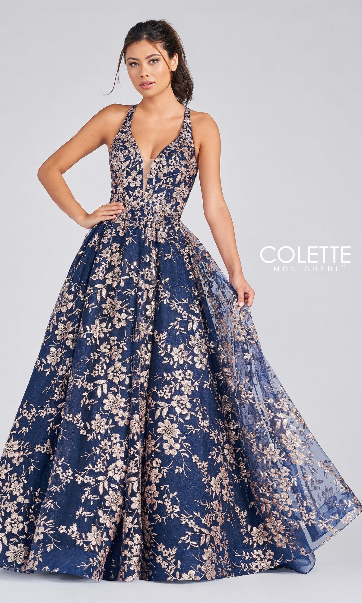 A woman poses in a sleeveless, floor-length Navy Blue Tulle Prom Dress with gold glitter print, featuring a deep V-neck and full skirt, against a plain light background.